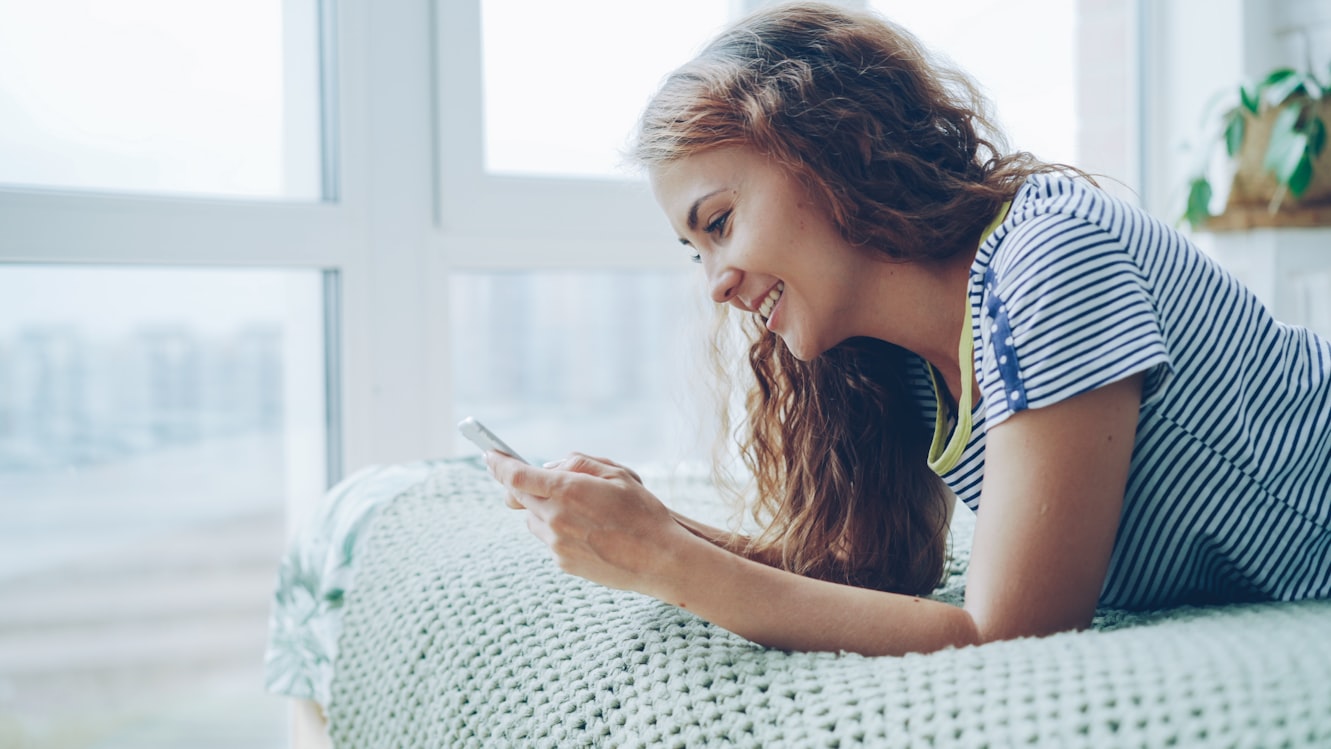 Young woman smiling warmly at her smartphone, illustrating emotional attachment to AI companion