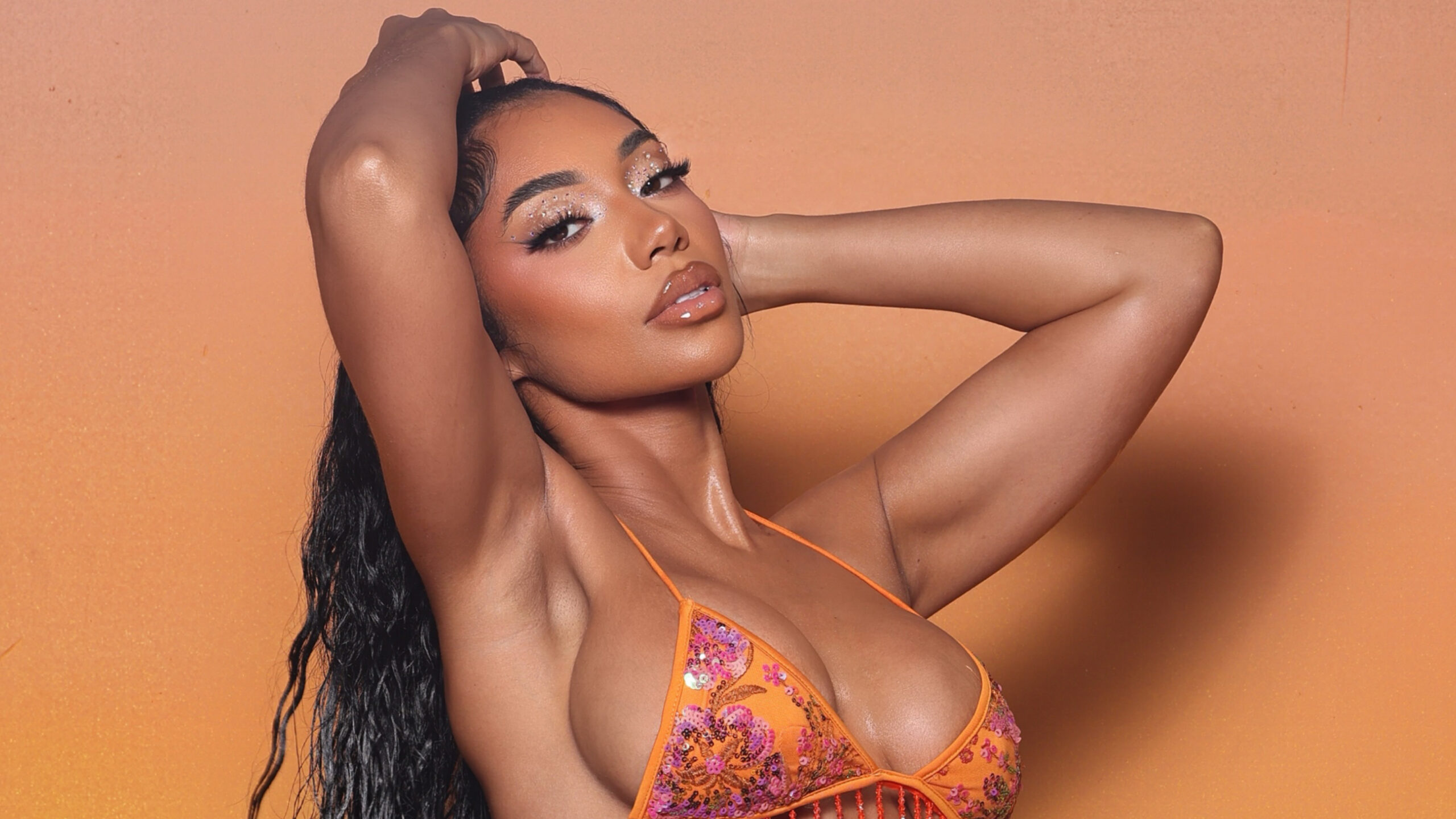 Autty Simone posing in an orange and pink embroidered swimwear bikini