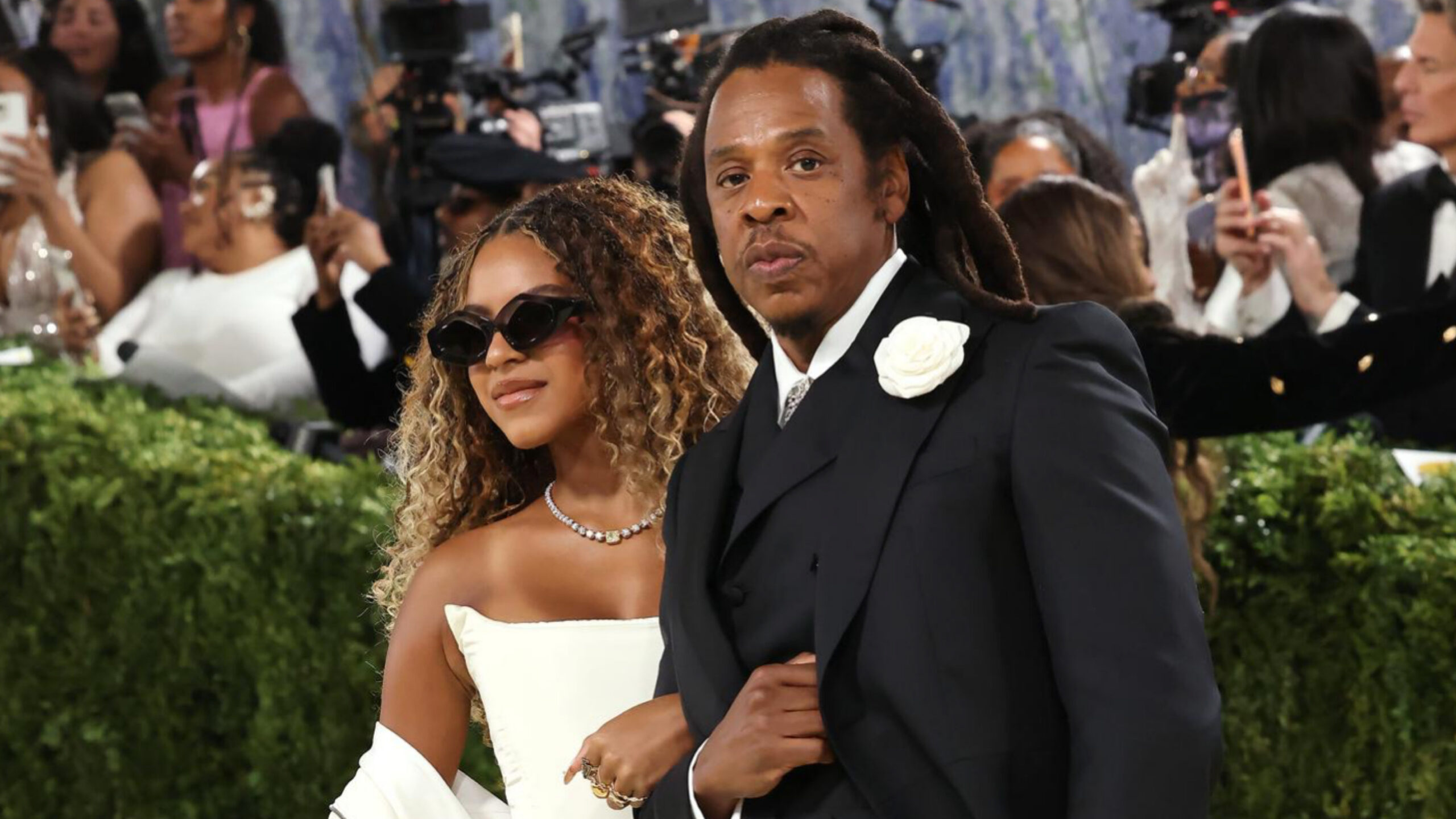 Jay-Z and Blue Ivy NYC Subway story featured image showing Jay-Z in a black suit and Blue Ivy Carter in a white dress and sunglasses at a red carpet event.