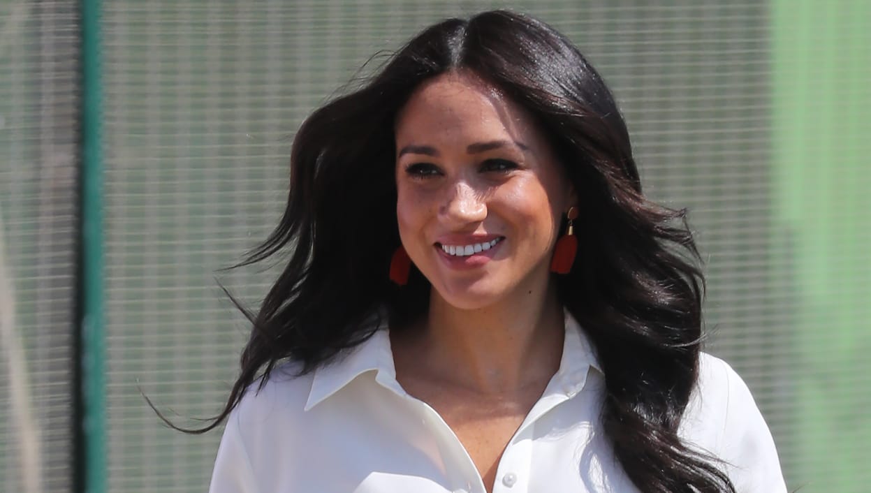 Meghan Markle wearing a white button-down gown outdoors.