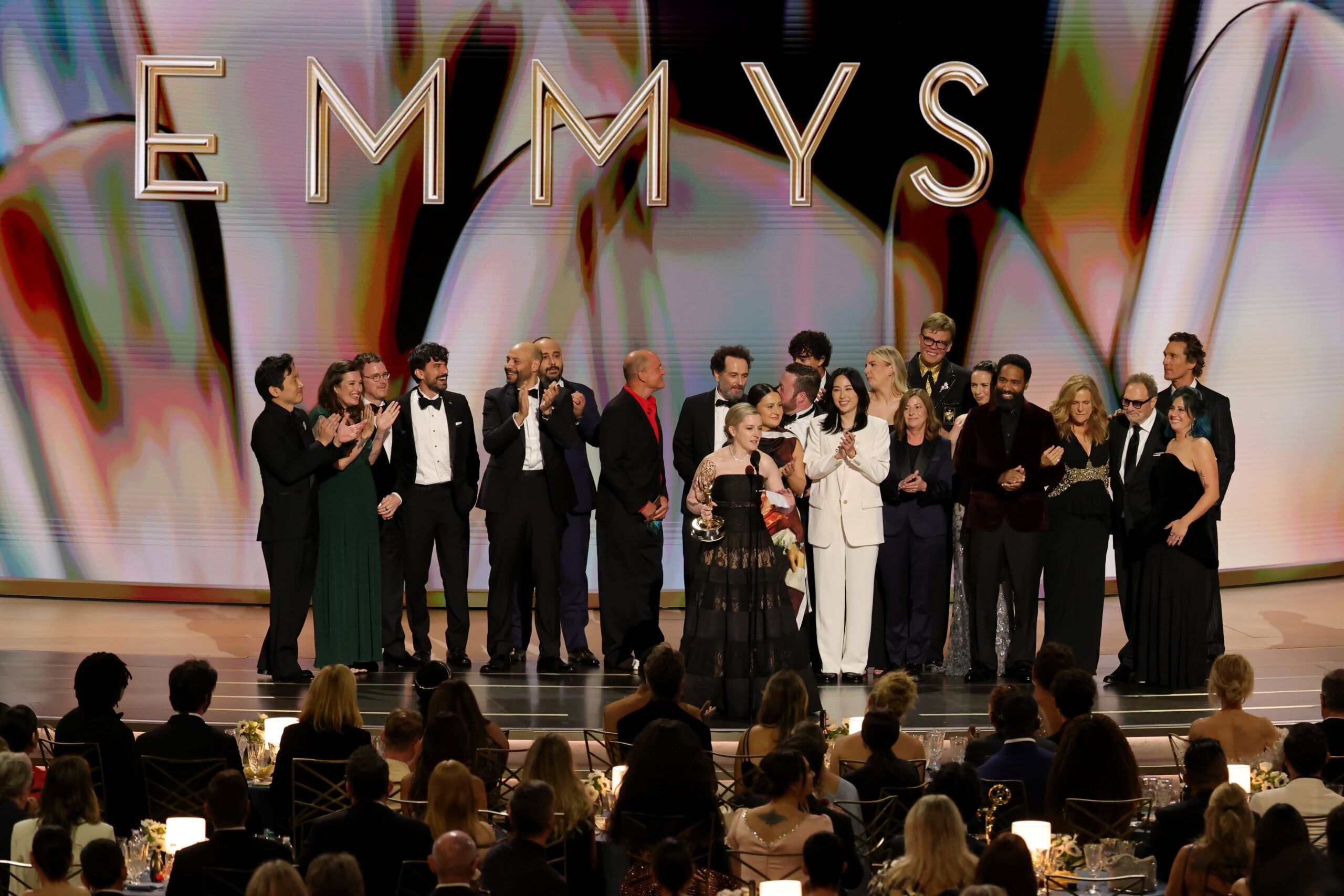 The cast and crew of a television show celebrating on stage after winning an Emmy Award.