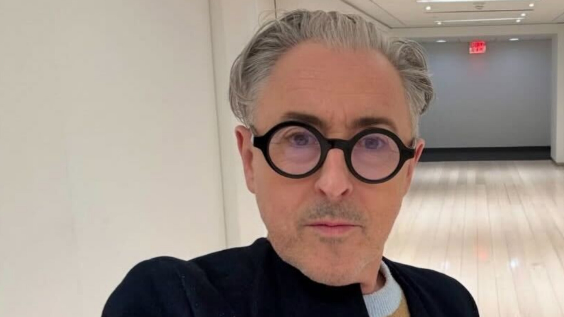 Actor Alan Cumming taking a selfie with round black glasses and swept-back gray hair.