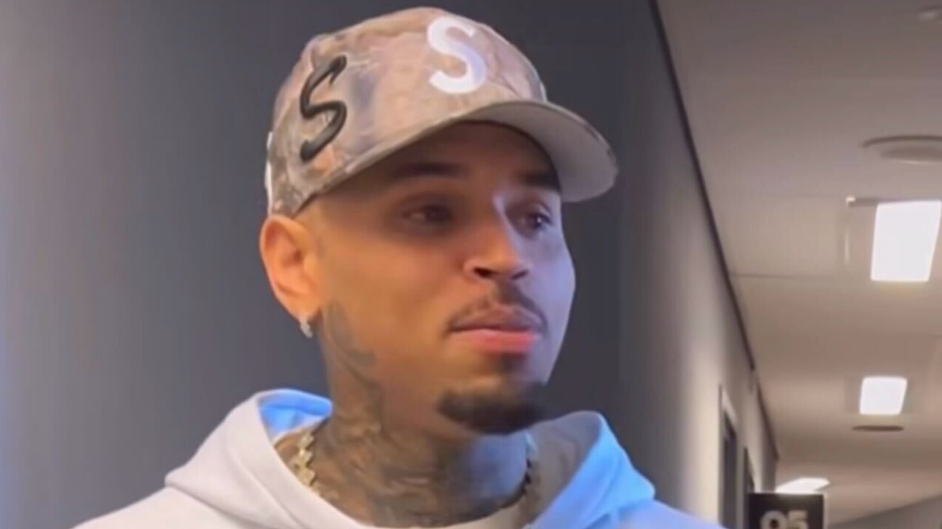 Chris Brown wearing a grey patterned Supreme cap and white hoodie.