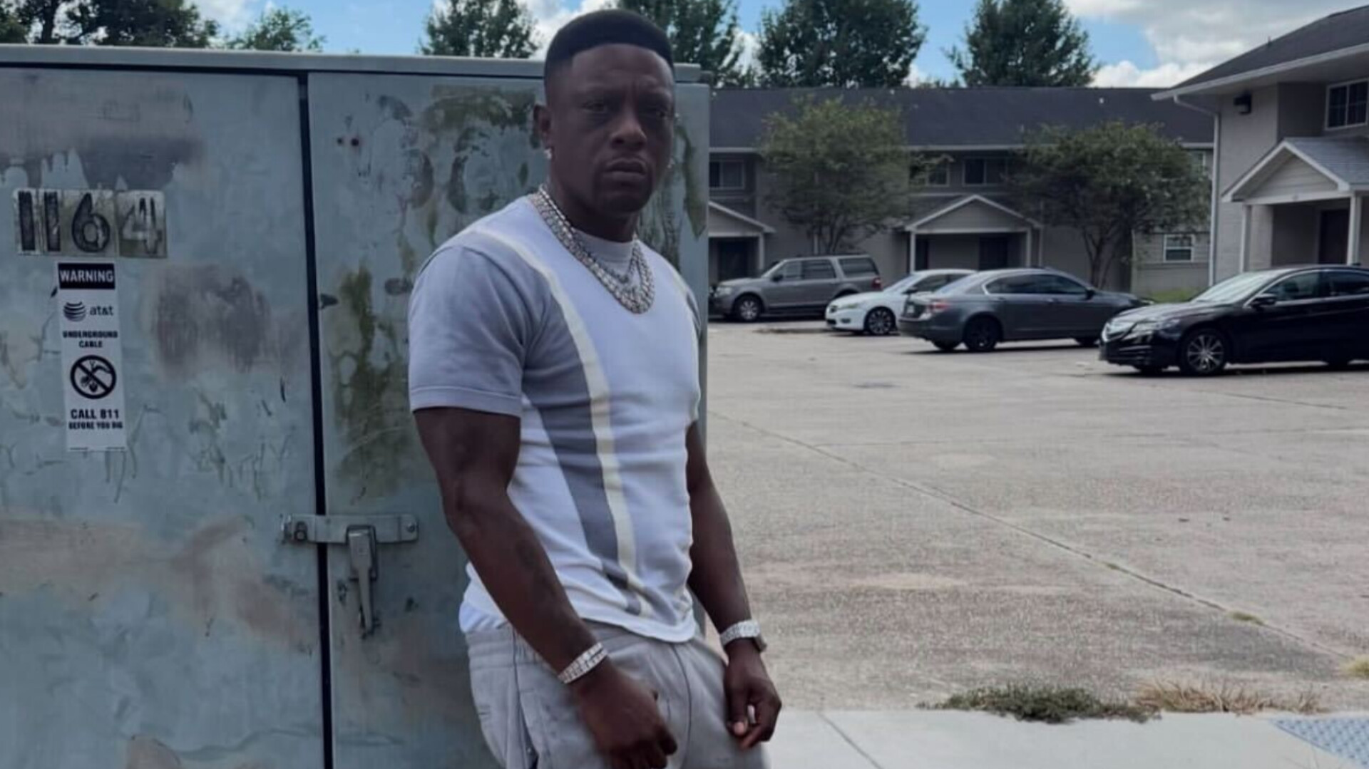 Rapper Boosie Badazz posing outdoors in a white and gray shirt near a parking lot.
