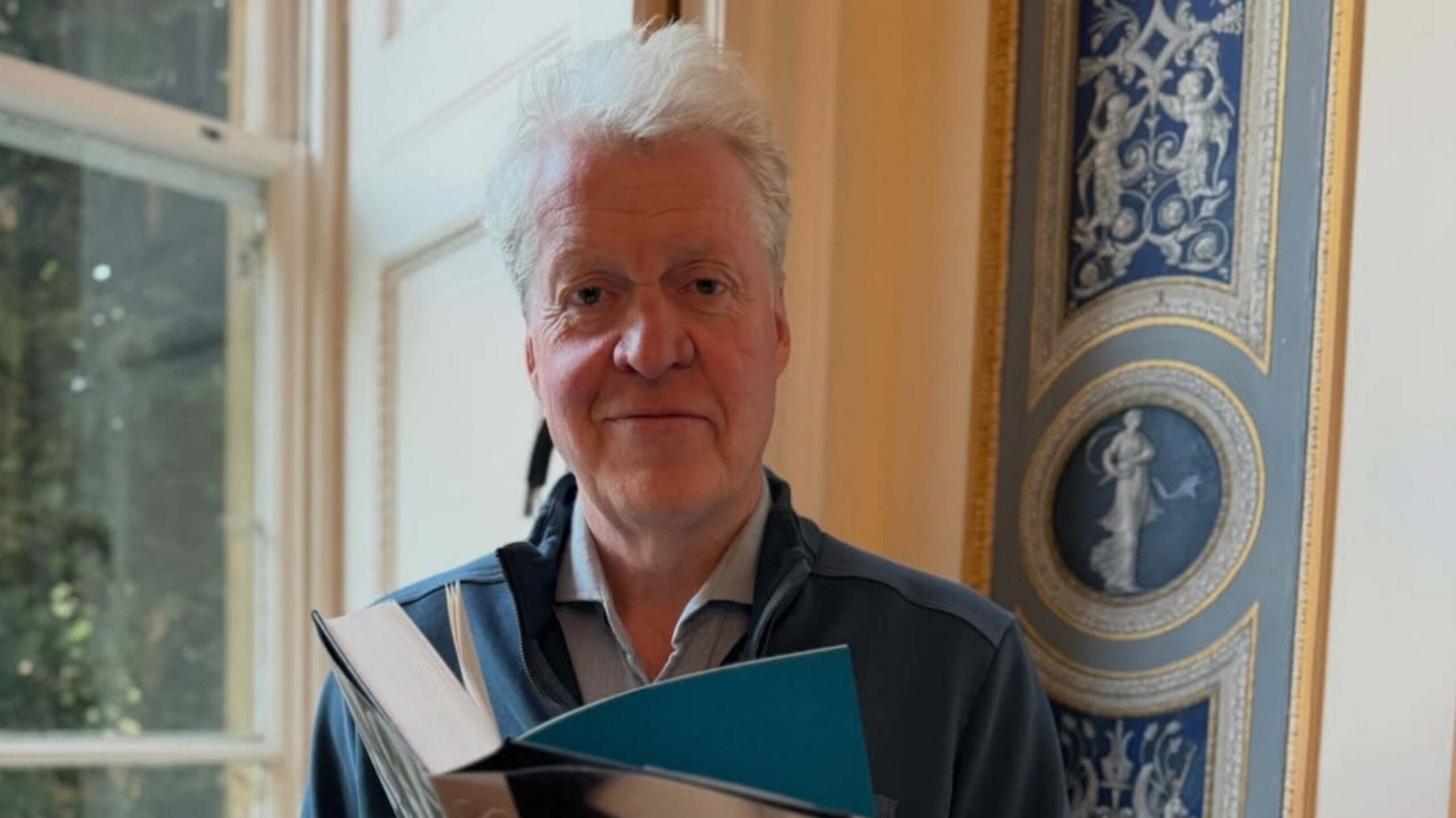 Charles Spencer, 9th Earl Spencer, holding an open book indoors.