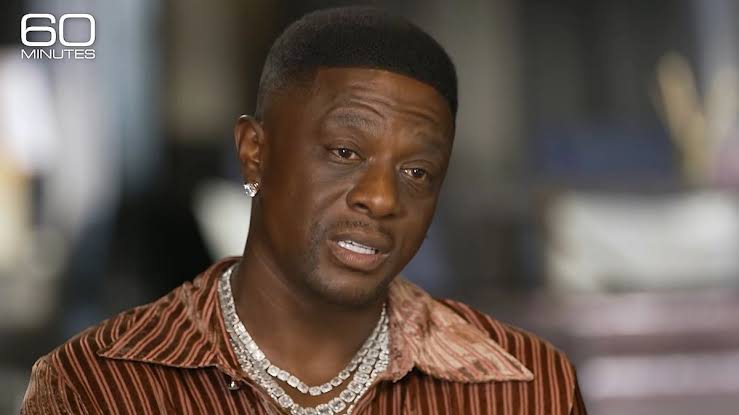 Close-up interview shot of rapper Boosie Badazz looking slightly off-camera with a serious expression. He has short hair, a diamond stud earring, and multiple thick diamond tennis necklaces, set against a softly blurred interior background with the "60 Minutes" logo in the top left corner.