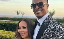T.I. and Tiny Harris posing together outdoors, with T.I. wearing a patterned black-and-white suit jacket and sunglasses.