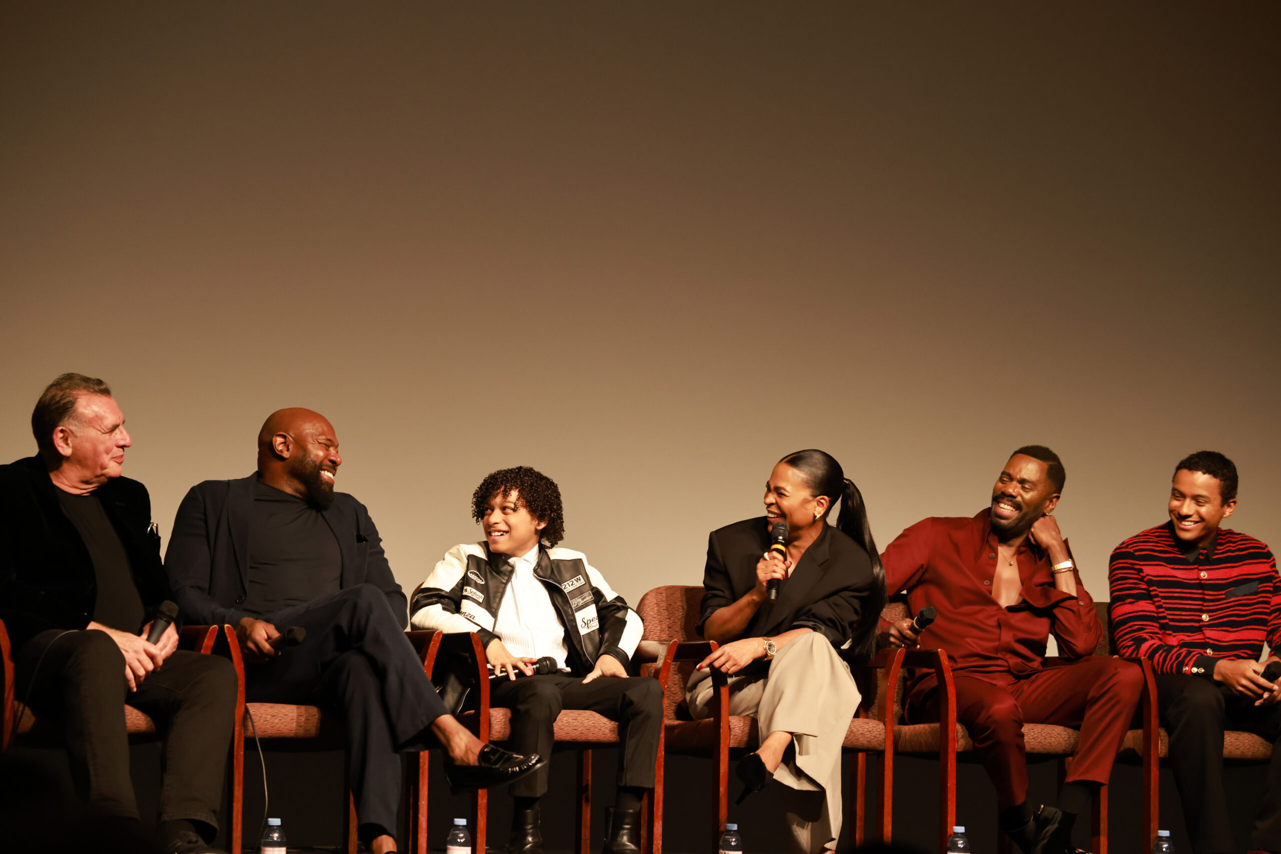 A panel of six people laughing and speaking into microphones during a stage discussion or Q&A session.