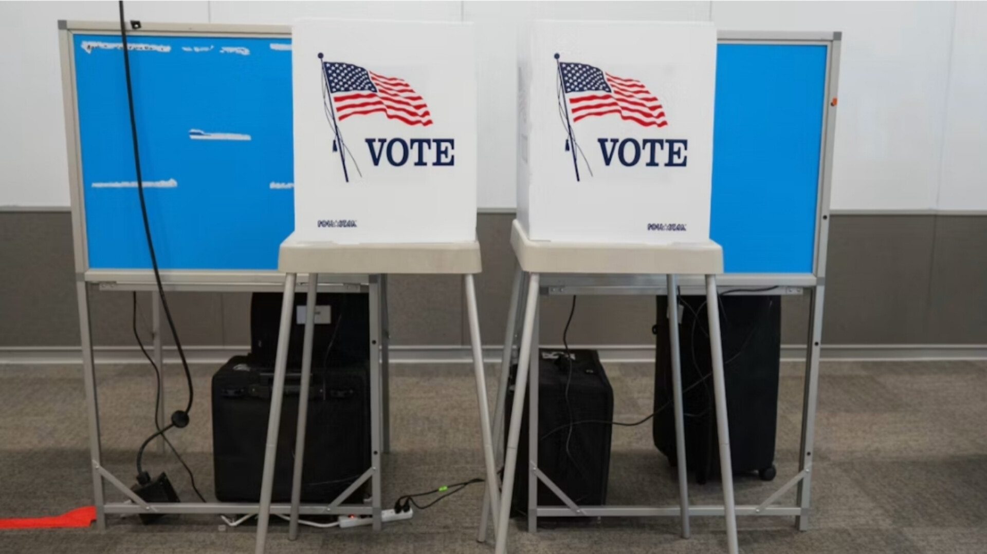Two empty voting privacy booths set up with American flag graphics and "VOTE" lettering inside a polling station.